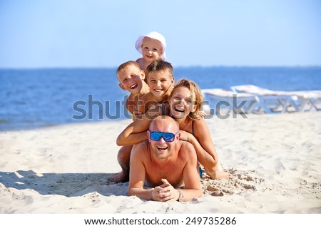 Happy mother and father with three children lying on the sunny beach.