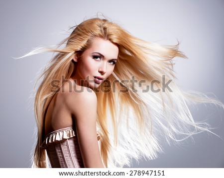 Beautiful young woman with long blonde hair. Pretty model posing in the studio on a black background with flying hair.