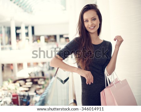 Happy beautiful woman with shopping bags stands at shop. Attractive caucasian girl with purchasing bags in big mall