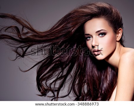 Portrait of the beautiful  young woman with long brown  hair posing at studio over dark background
