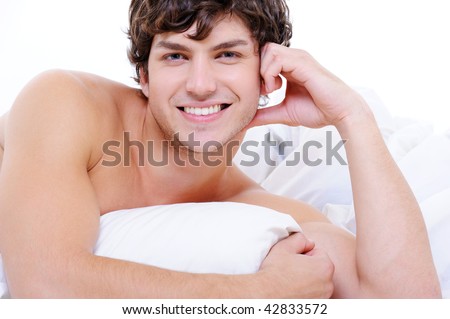 Attractive  sexy smiling young nude man lying in bed with pillow