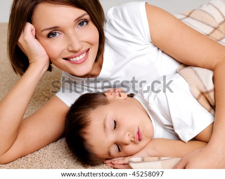Portrait of the happy mother to the sleeping small son who is covered by a warm plaid