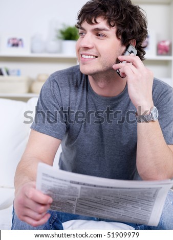 Portrait of handsome young man speaking on the phone and holding newspaper