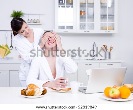 Two loving flirting people with laptop in the kitchen - indoors