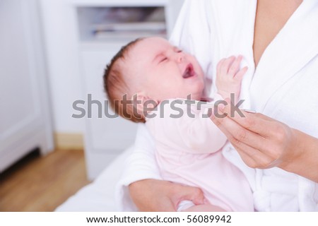 Portrait of screaming newborn baby with thermometer in the had of nurse - indoors