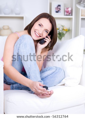 Portrait of beautiful young woman sitting on the sofa, speaking on the phone and making pedicure