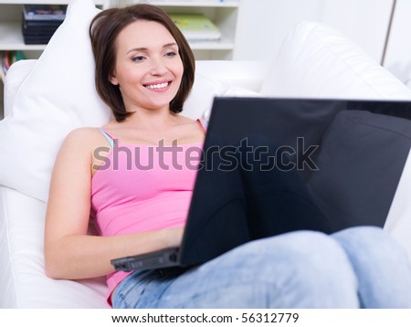 Beautiful happy resting woman lying on sofa with laptop at home