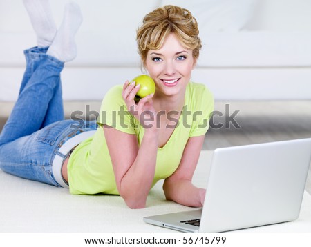 Woman with green apple and laptop lying on the floor - indoors