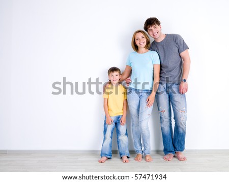 Happy young family with little son standing together in casuals near the empty wall - indoors