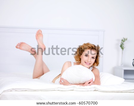 Relaxation for young beautiful smiling woman lying in a bed with pillow - indoors