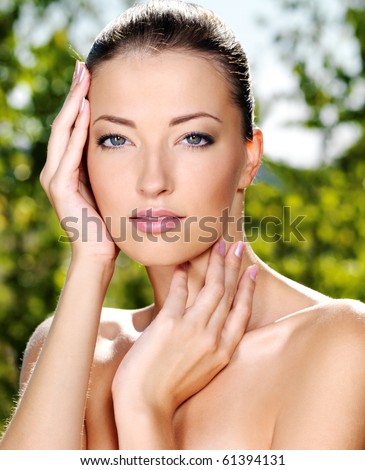 Beautiful sexy face of an young woman with fresh health skin. Female posing on the nature. Model stroking her body.
