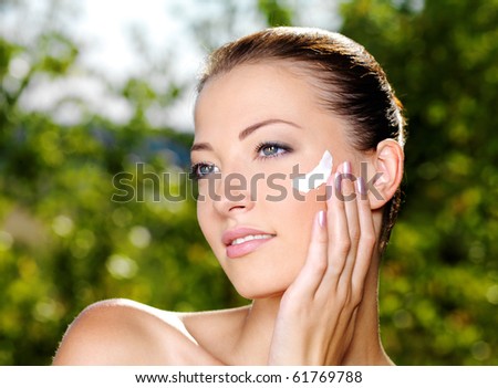 Beautiful sexy woman with fresh health skin applying cream on cheek. Adult girl on nature
