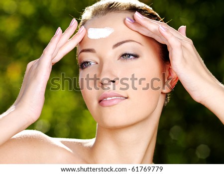 Beautiful sexy woman with fresh health skin applying cream on forehead - Outdoors