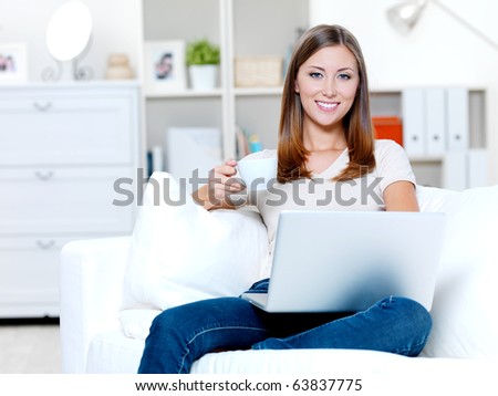 Beautiful smiling young woman with laptop and cup of coffee on the sofa