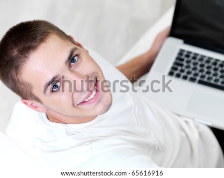 happy young guy using laptop and lying on the sofa - high angle