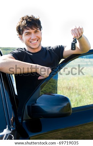 Successful young happy man showing the keys standing near the car