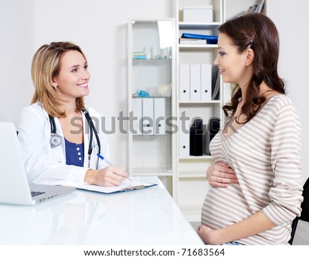 Consultation of young pregnant woman with her doctor - indoors