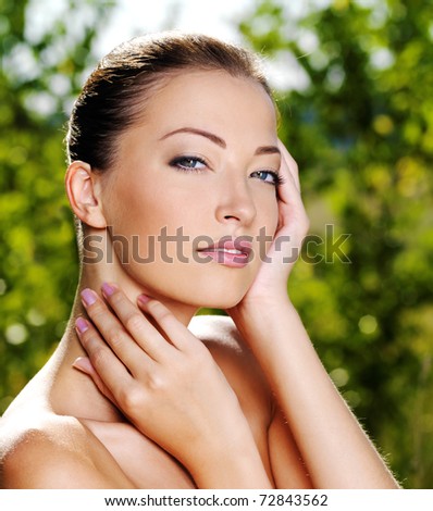 Beautiful sexy face of an young woman with fresh health skin. Female posing on the nature. Model stroking her body.