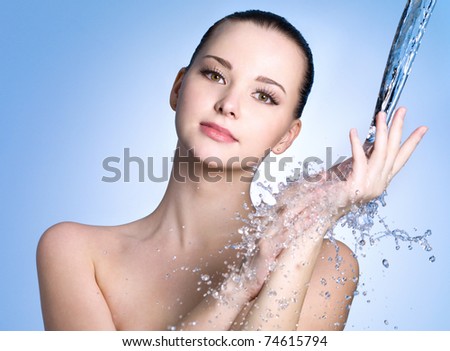 Beautiful healthy woman under stream of water falling on her hand- blue background