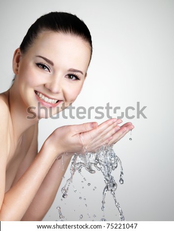 Beautiful smiling young woman washing her face with water - studio shot