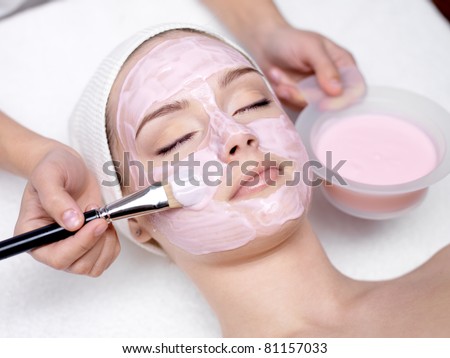 Young beautiful girl receiving pink facial mask in spa beauty salon - indoors