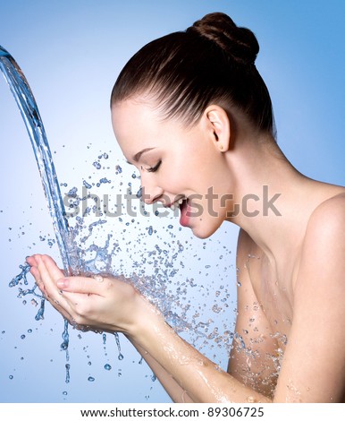 Young woman washing face under the stream of water - blue background