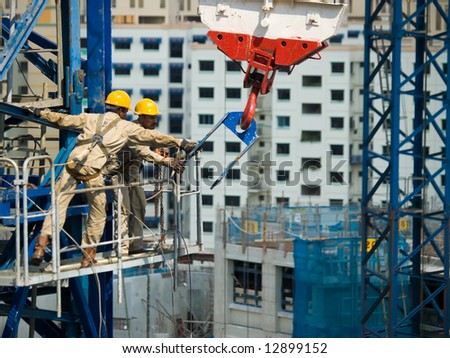 Workers reining in a tower crane\'s hook during the construction of its height extension