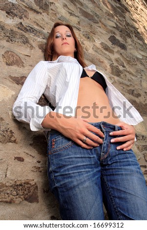 Young female dressed in white blouse and black brassiere pose in front old wall