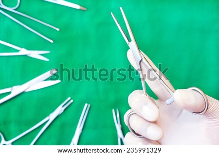 hands with gloves holding a long clamp surgery