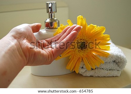 hand catching soap from soap dispenser with flower and hand towel