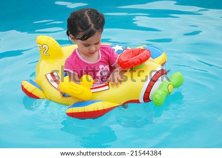 Cute toddler girl floating in a toy plane inflatable in swimming pool playing with a rubber ducky