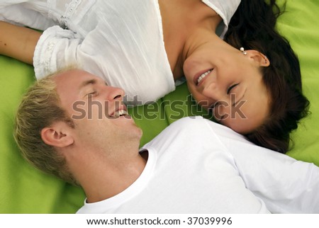 A young cute couple lie down beside each other on a picnic blanket with camera focused on the man.
