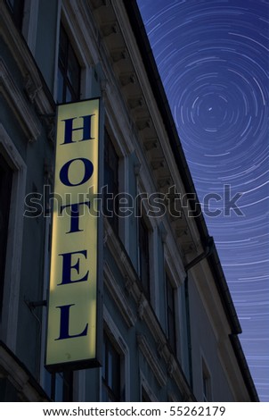 An lit neon hotel sign situated next to room windows at night with blurry star trails in the background sky to indicate the passing of time as you sleep.