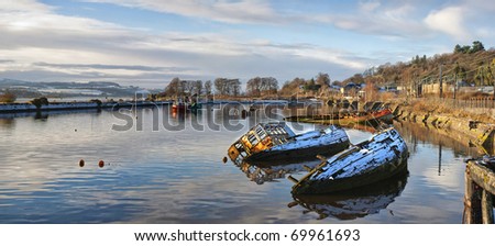 A panoramic image of sunken fishing boats lined up in the scottish harbour at Bowling.