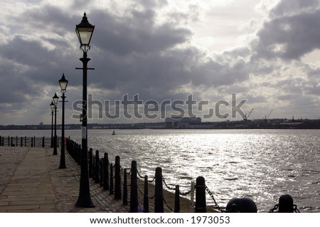 Street lights along the pier-head alongside the River Mersey as it runs through the city of Liverpool. Docks can be seen on the opposite side of the river.