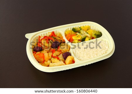 Cod a Portuguese style, rice and steamed vegetables in a package for frozing food. Package on a brown background.