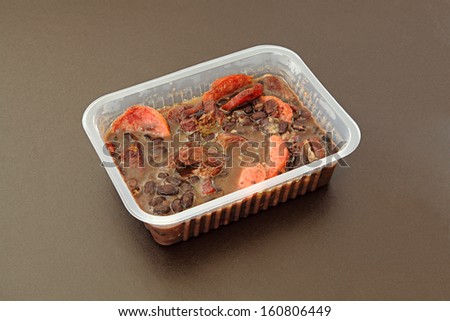 Brazilian Feijoada in a package for frozen food or to go. Package on a brown background.