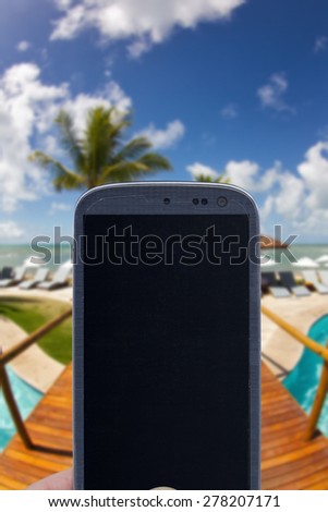 Smatrphone and a landscape. Idea of taking shots, accessing apps, Internet, blogs and others. The blur image is a sunny day at Arraial d\'Ajuda Eco Resort in Bahia - Brazil.