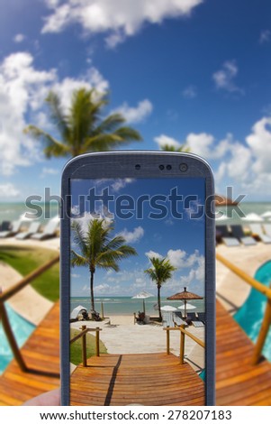 Smatrphone and a landscape. Idea of taking shots, accessing apps, Internet, blogs and others. The blur image is a sunny day at Arraial d\'Ajuda Eco Resort in Bahia - Brazil.