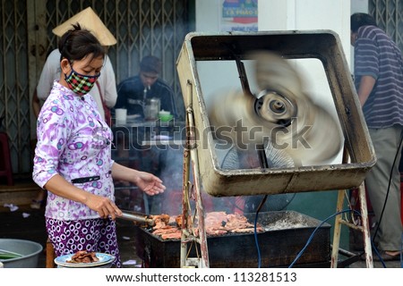 MY THO, VIETNAM - FEBRUARY 13: Vietnamese woman with face mask cooks on the street on February 13, 2012 in My Tho, Vietnam. My Tho is the regional market for fish and seafood.