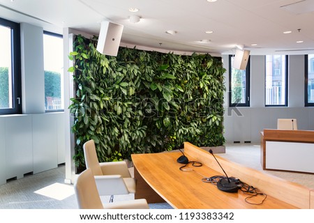 Living green wall, vertical garden indoors with flowers and plants under artificial lighting in meeting boardroom, modern office building