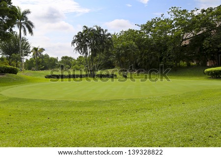 Landscape of a green golf field with trees and a bright blue sky