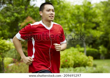Male sport fitness model with sweat listening to music with earphones in the park