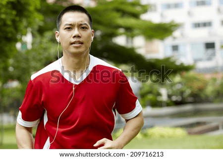 Male sport fitness model with sweat listening to music with earphones in the park