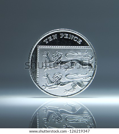 Shiny New Ten Pence UK Coin balancing on white surface. Finance and money concept