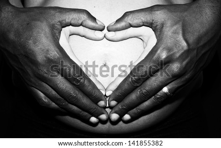 Portrait of a Couples hands making heart shape over her pregnant belly