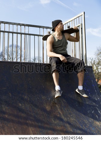 Portrait of a male skateboarder sitting on a half-pipe