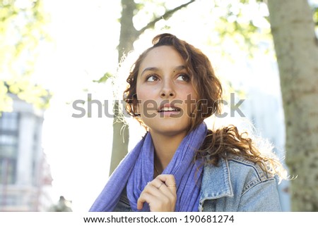 Portrait of a positive attractive young woman tying her scarf and looking off camera on a bright sunny day