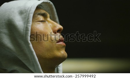 Hooded Asian man getting his breath back after an intense workout in urban environment