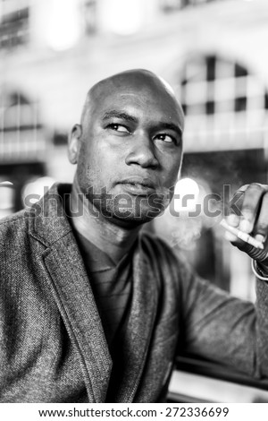 Portrait of a handsome african american man looking towards something off camera whilst smoking a cigarette in the city at night